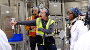 Tour guide explains demonstrates product manufacturing using hands-free audio tour headset.