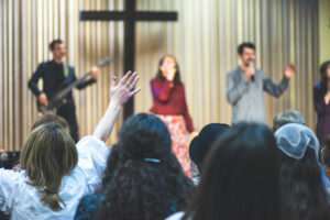 Church congregation with hands raised. Worship band in background.